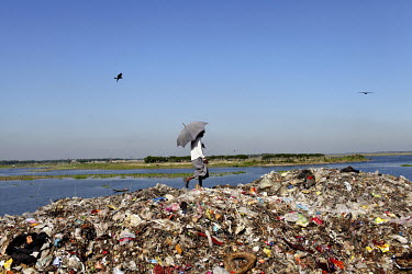 A man walking beneath an umbrella looking for recyclable material at the biggest rubbish dump in Dhaka. The city alone generates about 3500 to 4000 metric tons of solid waste each day.