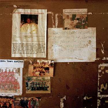 A handwritten notice with instructions on dealing with children in conflict with the law hangs beside a 'wanted for murder' poster and team pictures of a recent police football tournament on the notic...
