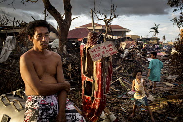 A man stands, among the devastation left by Typhoon Haiyan, beside a damaged statue of Jesus which has a sign attached to it that reads: 'Help us we have no food'. Typhoon Haiyan, or Yolanda as it is...