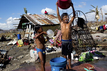 Children wash with water collected from a nearby well. Behind them a man tries to make a shelter from the devastation left after Typhoon Haiyan swept through the Philippines. Typhoon Haiyan, or Yoland...