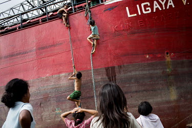 Children climb ropes on to a ship in order to scavenge items from the beached hulk. It was left sitting in a field near Tacloban city after Typhoon Haiyan swept through the Philippines. Typhoon Haiyan...