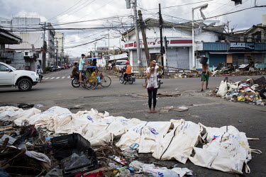 A woman covers her face as she stands by a row of bodies laid out for collection on a street corner in Tacloban after Typhoon Haiyan swept through the Philippines. Typhoon Haiyan, or Yolanda as it is...