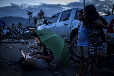 A man uses his laptop at a power source supplied by a mobile phone company in Tacloban city after Typhoon Haiyan swept through the Philippines. Typhoon Haiyan, or Yolanda as it is known in the Philipp...