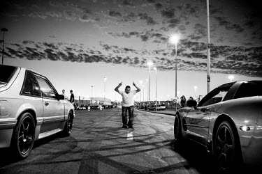 A man signals the start of a race during a 7th Street Sideshow, an illegal gathering of car and motorbike enthusiasts who come together to perform stunts and hold street drag races. In the Bay Area, d...