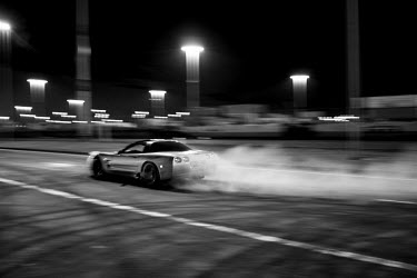 A car races along a road during a 7th Street Sideshow, an illegal gathering of car and motorbike enthusiasts who come together to perform stunts and hold street drag races. In the Bay Area, deep in Ea...