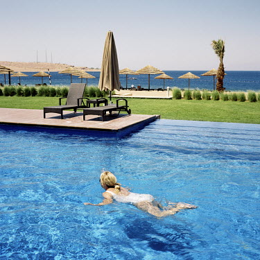 A tourist swimming in the pool at the Movenpick Hotel with the Gulf of Aqaba in the background.