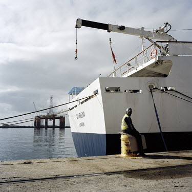 A dock worker in Cape Town sits on the harbour next to the RMS St Helena. There are only two remaining Royal Mail Ships, the other being Cunard's Queen Mary 2. The RMS St Helena is the only link to th...