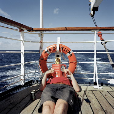 A passenger listens to a radio and reads a book while on the deck of the RMS St Helena. There are only two remaining Royal Mail Ships, the other being Cunard's Queen Mary 2. The RMS St Helena is the o...