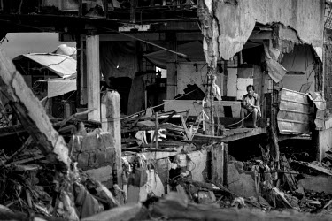 A man sits in the exposed interior of a building on the shoreline, where, following Typhonn Haiyan, all the structures were either completely destroyed or damaged beyond repair. Typhoon Haiyan, or Yol...