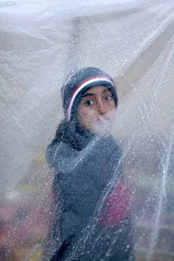 A Syrian refugee boy looks through a plastic sheet, covered in drops of rain, at Nizip 1 refugee camp.