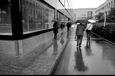 Businessmen and women, shelter from the rain beneath umbrellas, as they head to work in a newly developed banking quarter in the Acasias district. Pictet & Cie, private bankers are to the left and UBS...