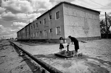A woman pumps water fropm a standpipe beside an apartment block. On the wall is the fading emblem of the 1980 Moscow Olympic Games.  During the 1950s and the 1960s the rivers that feed the Aral Sea (t...