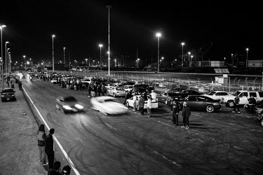 Cars race along a stretch of road with crowds of people looking on during a 7th Street Sideshow, an illegal gathering of car and motorbike enthusiasts who come together to perform stunts and hold stre...