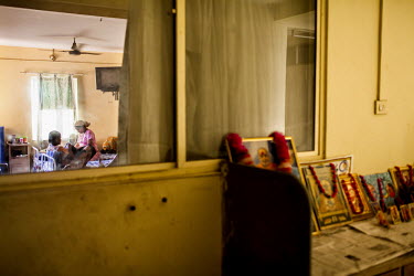 Images of a variety of deities and religious teachers line a shelf outside a room while surrogates pass their time doing embroidery and watching television in the surrogate's hostel on the 3rd floor o...