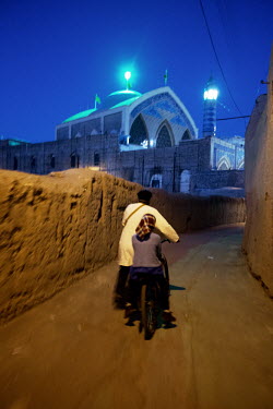 A man and a girl on a bicycle rides through a dark street near the Agha Bozorg Mosque.