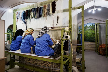 Three women weaving on a hand loom in a carpet factory.
