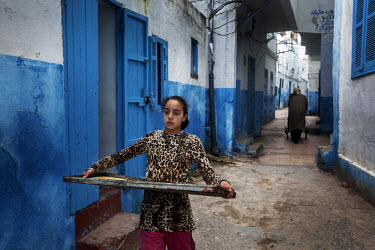 A young woman carries a tray of freshly baked bread along an alley where the buildings are all painted blue and white.