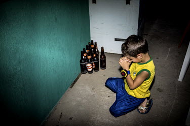 A boy kneels and prays before the penalty shootout between Brazil and Chile during the World Cup, which Brazil ultimately won 3-2. In the corner empty beer bottles stand lined up.