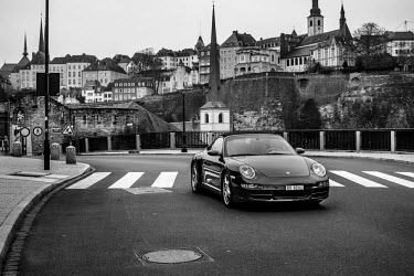 A man drives a Porsche along a city road.