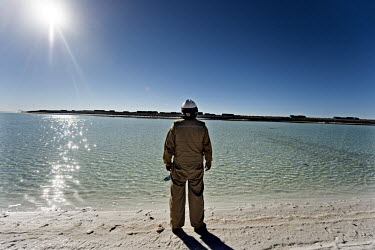 A worker at the lithium extraction facility standing on salt beside the surface water that is just five inches deep and made up of accumulated rainwater from the recently ended rainy season. Workers d...