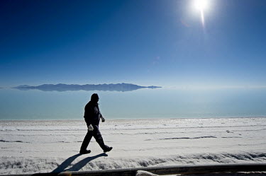 A worker at the lithium extraction facility traverses a raised causeway that cuts through the shallow surface water, 14km into Bolivia's Salar de Uyuni salt flat. The causeway provides access to the l...