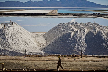 A worker strides past huge deposits of potassium chloride awaiting purification at a lithium extraction facility. Behind them are the pools, each measuring one square kilometre, in which the lithium i...