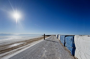 A worker at the lithium extraction facility traverses a raised causeway that cuts through the shallow surface water, 14km into Bolivia's Salar de Uyuni salt flat. The causeway provides access to the l...
