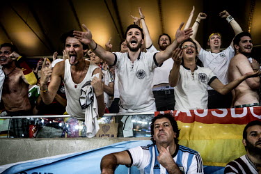 Fans of the Germany football squad cheer  their team at the Maracana stadium in Rio de Janeiro during the final match of the 2014 Football World Cup. An Argentina fan looks pensively below. Germany be...