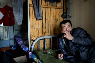 A coal miner smokes a cigarette while lying on a bed in his dormitory at the Datong Coal Mine Group's (Tong Mei) Tong Xiu coal.