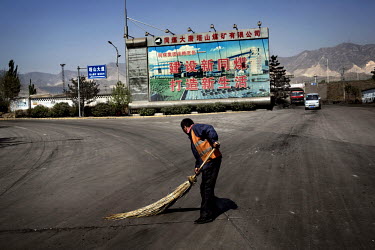 A worker sweeps coal dust off a road at the Datong Coal Mine Group's (Tong Mei) Tashan Coal Mine complex. Behind him a billboard with a propaganda slogan reads: 'Build Up Tong Mei & Build Up New Life'...