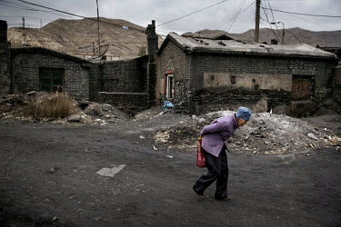 An elderly woman walks through a run down housing community and coal yard near the Datong Coal Mine Group's (Tong Mei) Yong Ding Zhuang coal mine.