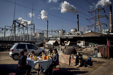 The family of migrant construction workers eat a meal at a wedding banquet in their housing compound. Looming over them are the smoke stacks and pylons of the Datong No. 2 coal fired power plant, wher...