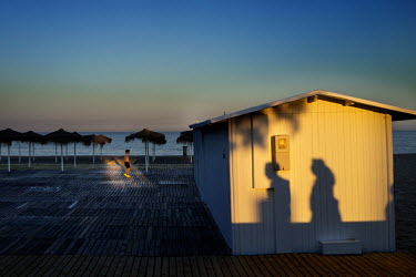 The shadows of people walking a seaside promenade fall on a shed Fuengirola. The long broad beach, stretching from Fuengirola, is crowded with tourists during the day throughout the summer months but...