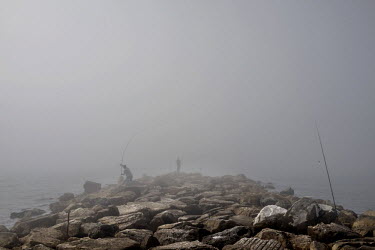 People fishing from a water break at Torreblanca, are enveloped by morning fog. The long broad beach, stretching from Fuengirola, is crowded with tourists during the day throughout the summer months b...