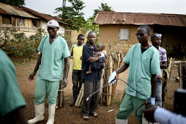 Residents of the village of Teldou watch as MSF (Doctors Without Borders) staff, wearing protective clothing, disinfect a nurse from a private clinic in the village. An Ebola virus epidemic of unprece...