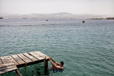 A man holds on to a jetty that extends into the Red Sea from the shore.