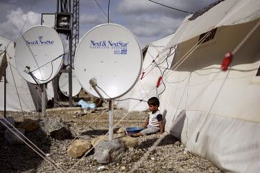 A Syrian child sits beside satellite dishes in Islahiye Refugee camp.