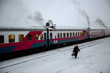An elderly woman who sells food to passangers on passing trains walks alongside the Matvei Mudrov at Selikhin.   The Matvei Mudrov train is a medical train operated by Russian Railways along the cours...