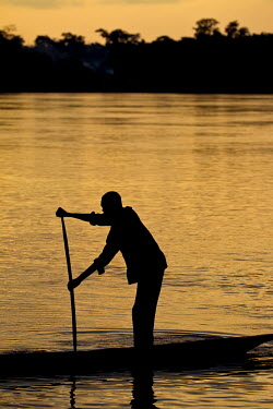 A man paddles his dugout canoe at sunset on the Congo River.