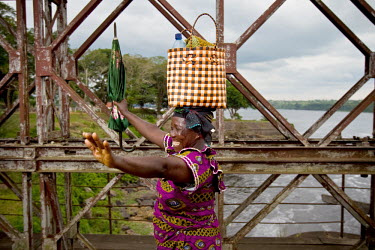 A woman laughs while crossing a bridge over the Tshopo River in Kisangani, carrying a basket on her head.
