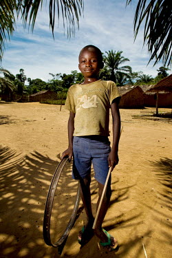 A boy holds a bicycle wheel rim that he uses as a toy by pushing it along with a stick.
