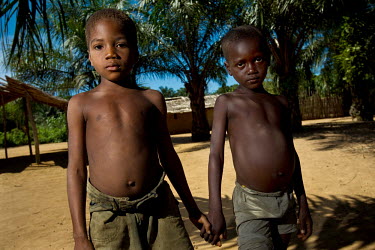 Two children hold hands while they stand together in the village centre.
