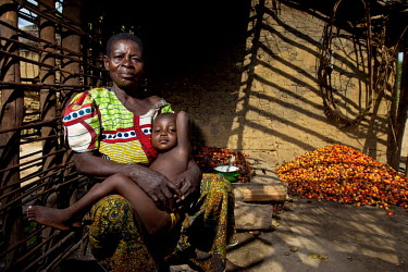 A woman and her child sit together in a  room where palm nut fruits are stored.