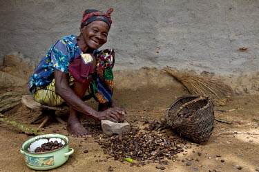 An elderly woman cracks palm nuts with a stone.