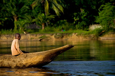A boy sits in the prow of a dugout canoe as it makes its way along the Congo River