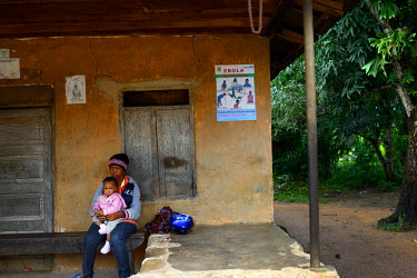 A woman sits near a checkpoint with her baby below a sign which tells people about the effects of the Ebola virus. She is unable to leave the quarantine area near the town of Kenema in eastern Sierra...