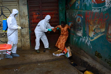 Emergency health workers help a woman suspected of being infected with Ebola who was lying in an open sewer along the main street in Freetown. Emergency health services took hours to assist the woman...