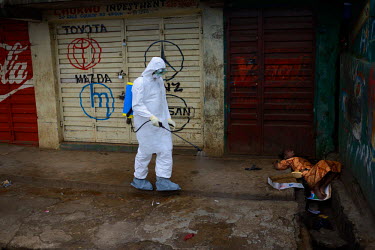 An emergency health worker sprays chlorine next to a woman suspected of being infected with Ebola who is lying in an open sewer along the main street in Freetown. Emergency health services took hours...