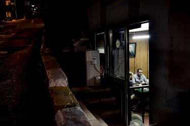 A man, seen through the doorway at a working mens club in the Topanae district, smokes a cigarette while playing a game of cards.