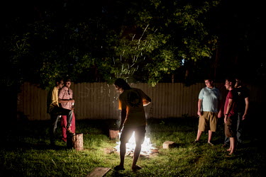 A gathering around a garden fire of young people at a house party on a Saturday night.